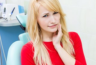 Woman in dental chair holding cheek