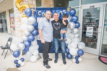 Two men and little boy smiling in front of balloons