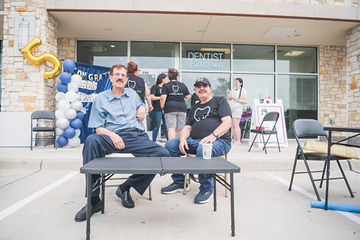 Two men sitting at a table in a parking lot