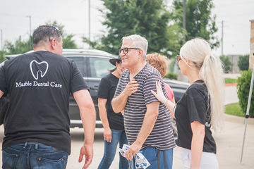 Dental team members talking to older person with glasses and striped shirt