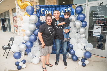 Man and woman with little boy smiling together at celebration of dental practice's anniversary