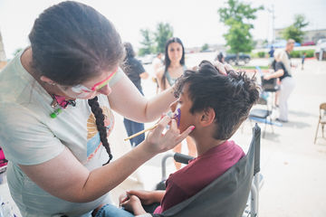 Little boy sitting in chair while woman paints his face