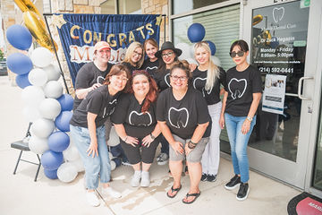 Dental team wearing matching shirts gathered in front of dental office