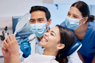 Patient smiling at reflection in mirror next to dental team