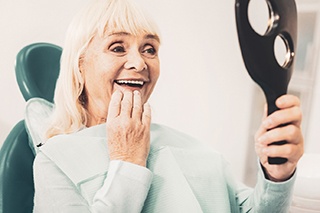 A senior woman admiring her dentures in a hand mirror