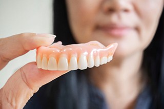 A close up of removable dentures held by a woman