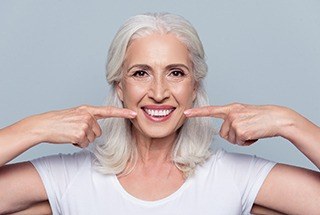 Woman smiling and pointing at her dentures in McKinney