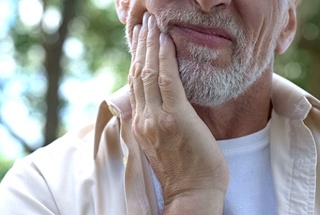 Man in need of dental implant salvage in McKinney puts hand on cheek