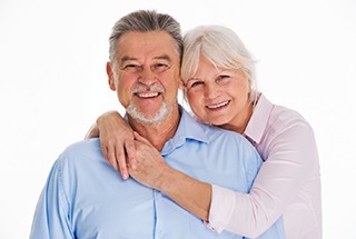 Older couple smiling with woman’s arms around man