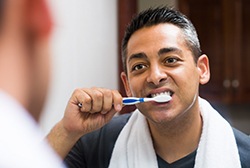 Man with greying hair looking in the mirror while brushing his teeth