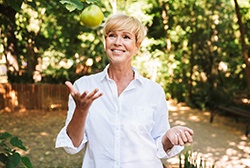 Woman smiling while tossing up green apple while outside