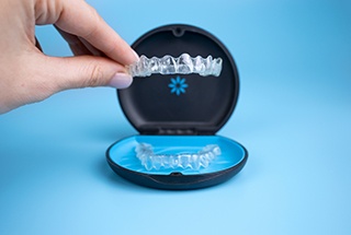 Fingers lifting upper Invisalign tray out of its carrier case with blue background