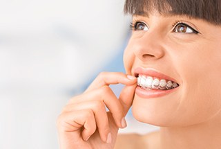 profile view of woman with brown eyes pulling Invisalign off upper arch