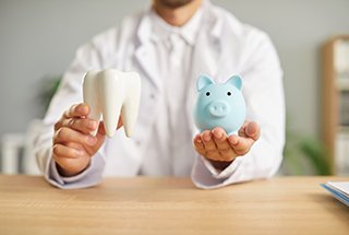 Headless dentist in white coat holding model tooth and blue piggy bank