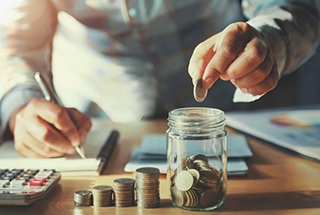 Man dropping a coin into a jar on his desk