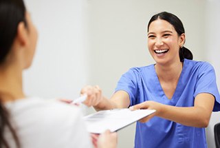 Dental assistant handing a patient a dental insurance form