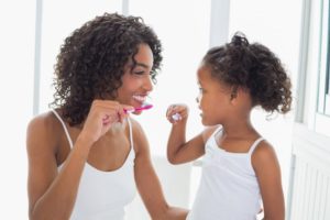 Smiling mother teaching her young daughter how to brush her teeth