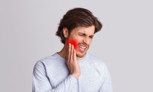 Man in gray shirt holding jaw in pain